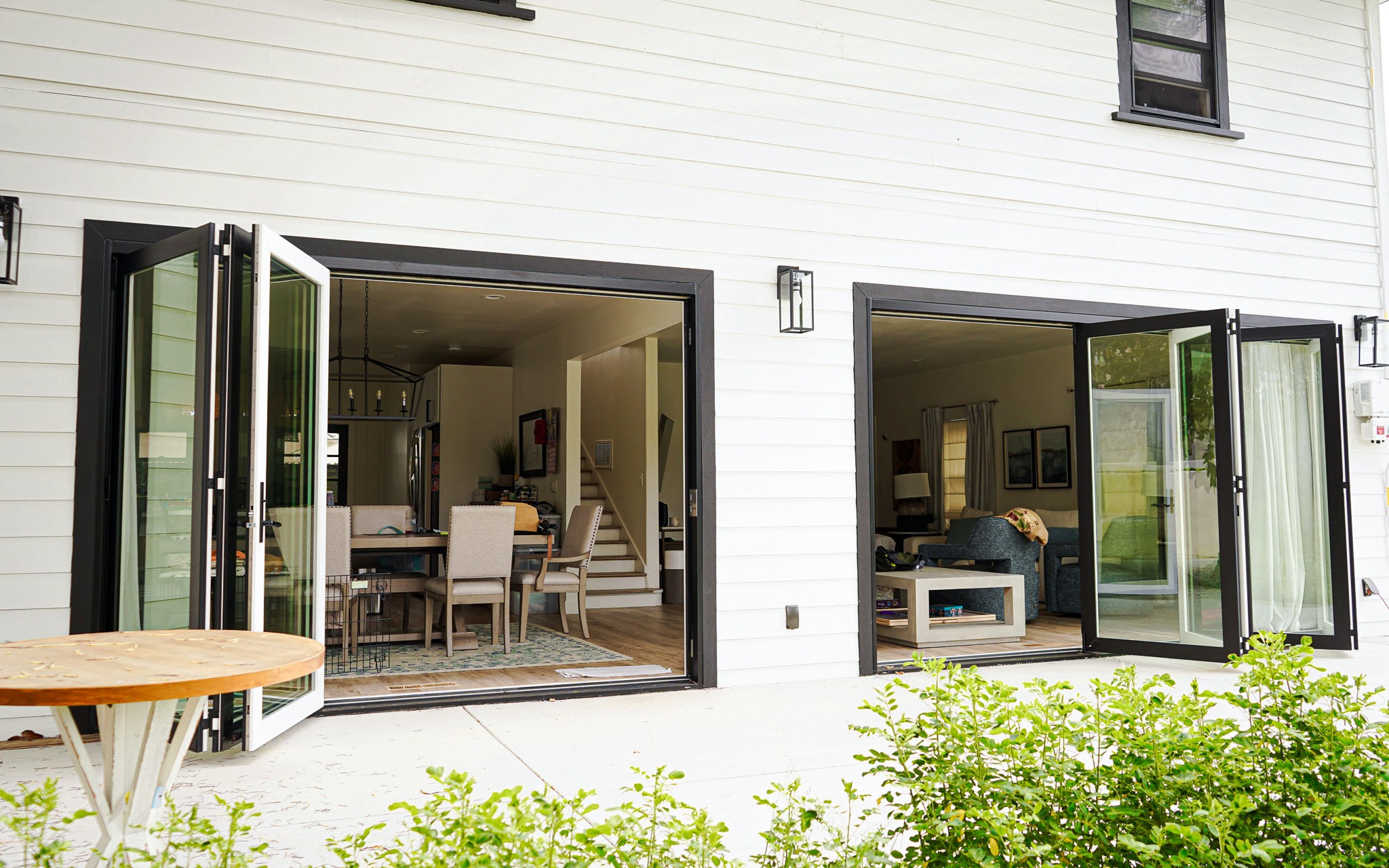 Modern house with open folding glass doors leading to a stylish living and dining area, viewed from an outdoor patio.